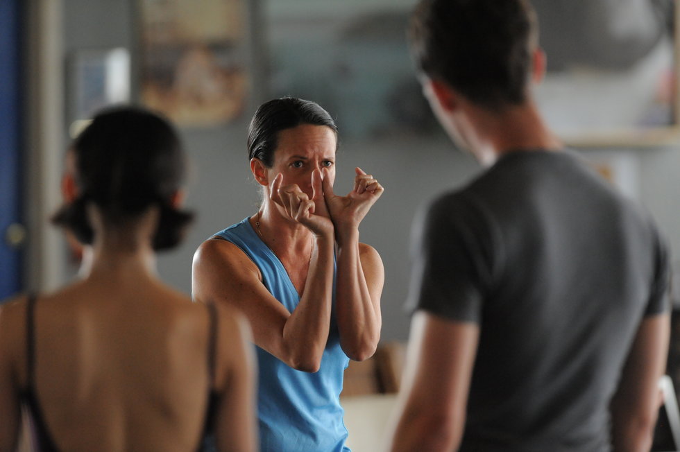 Seiwert, in a blue tank top, demonstrates a gesture to her dancer using both of her hands.