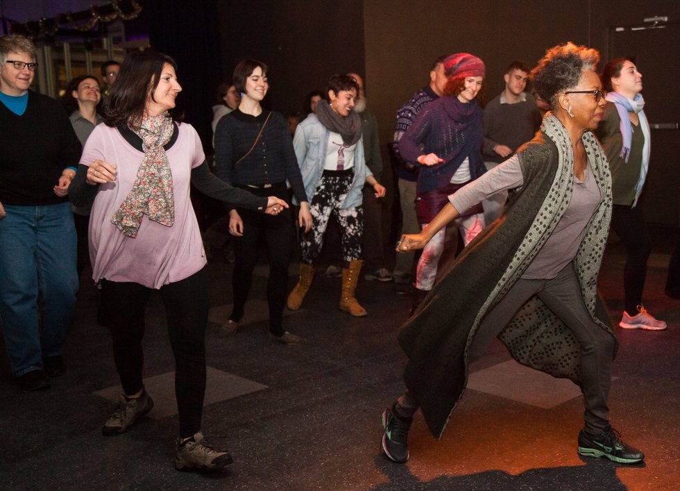 Zollar leads a dark room full of adults in a dance class by demonstrating in a low lunge