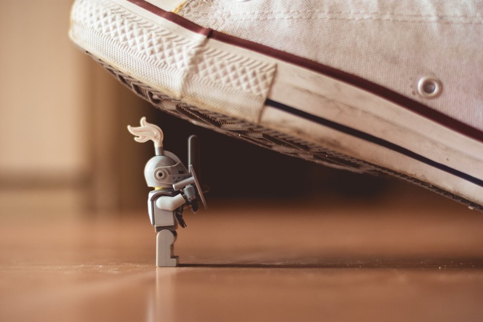 Small lego knight holding a sword and shield with a human foot about to step on it.