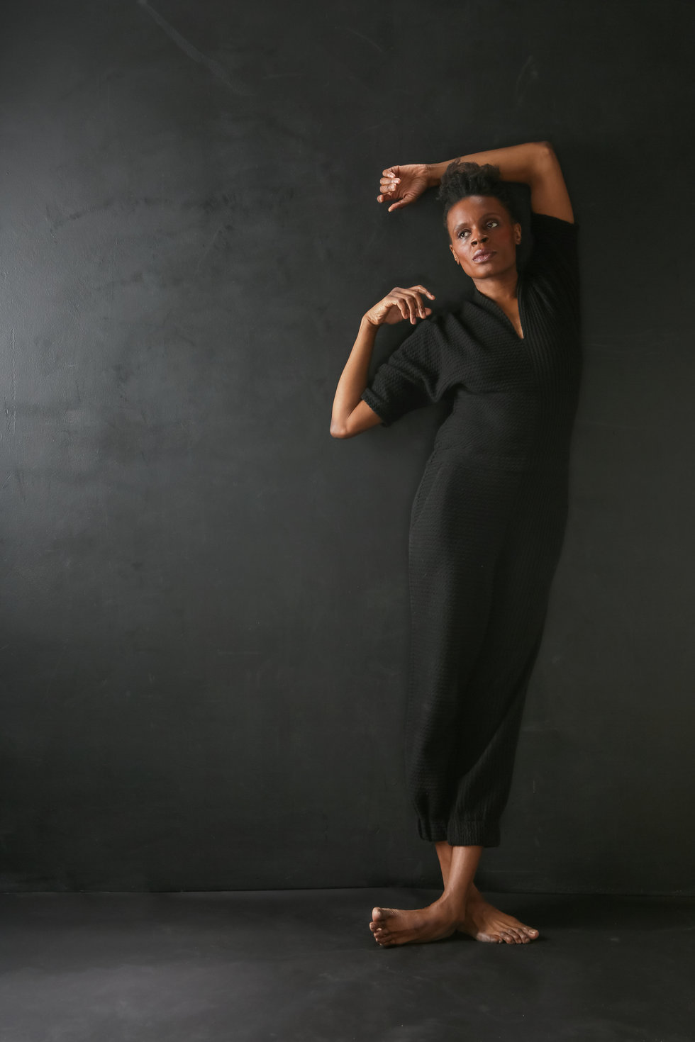 Okwui Okpokwasili leans against a dark background, one foot crossed over the other