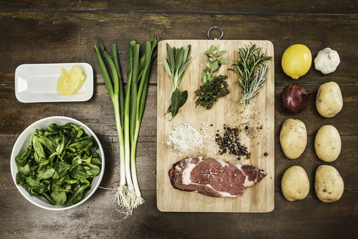 raw meat and vegetables on a wooden chopping board
