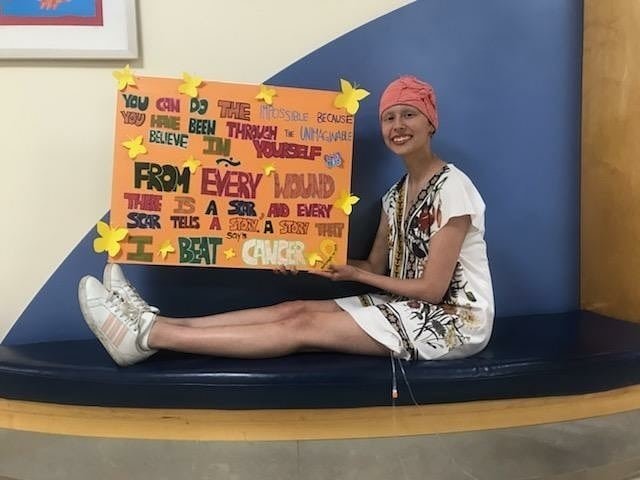Chiara Valle, on her last day of chemo, shows a poster of inspirational text that ends with, "I beat cancer."