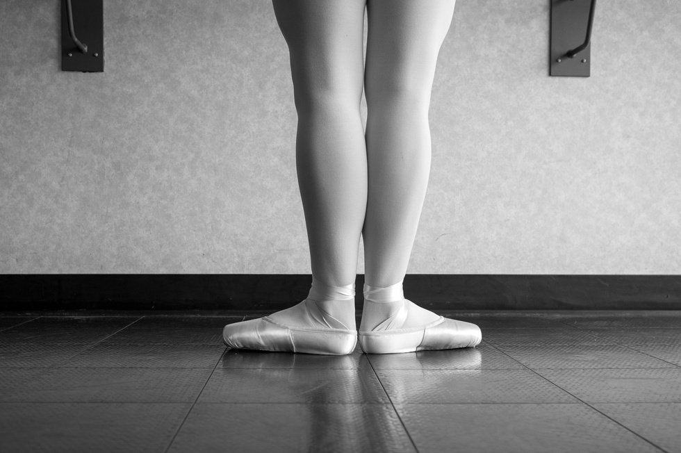Black and white version of back view of ballet dancer ballerina at the barre in dance class standing in first position