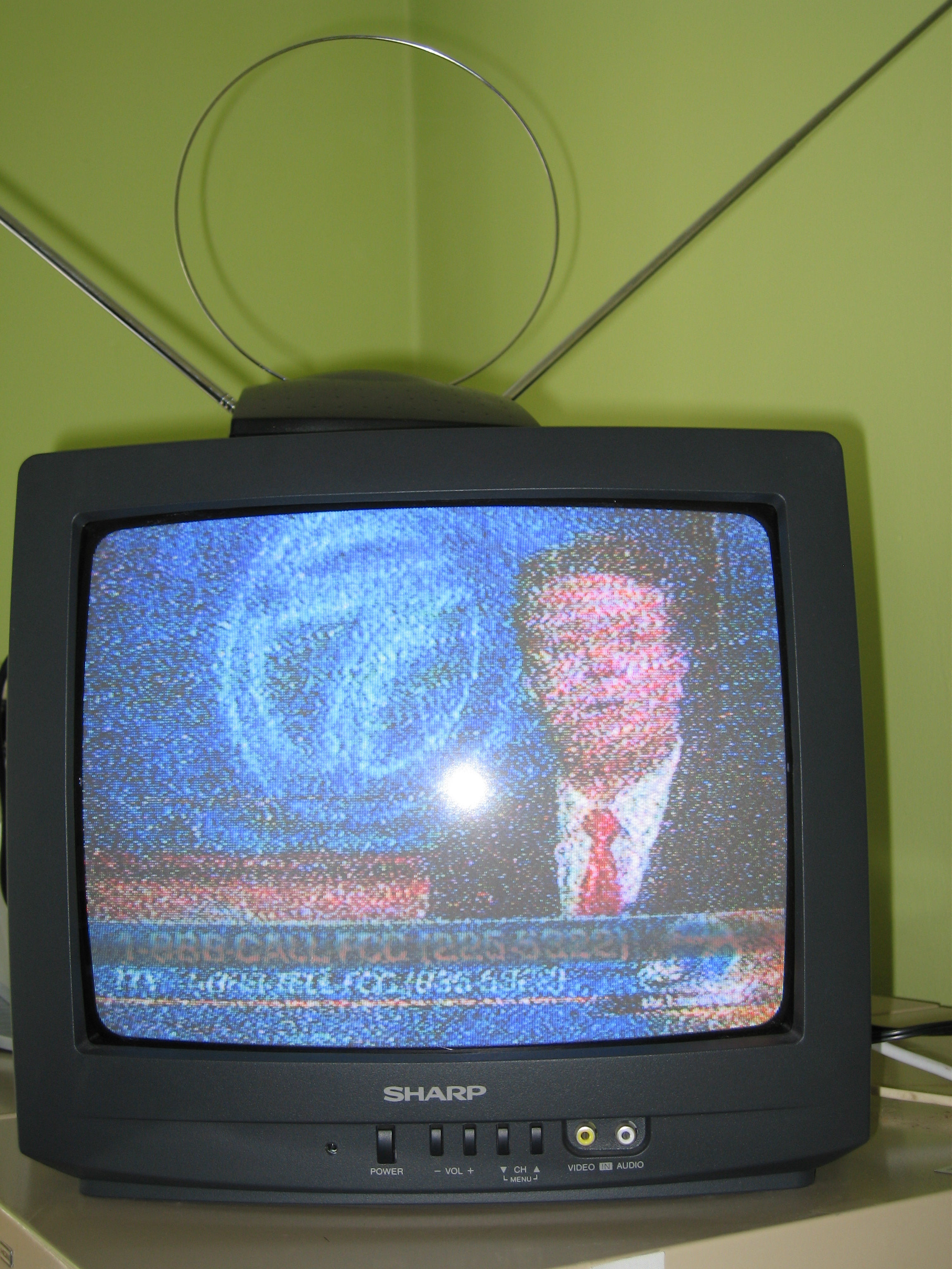 An old analog TV displaying a news reporter speaking during a news program. The graphics is very blurry. 