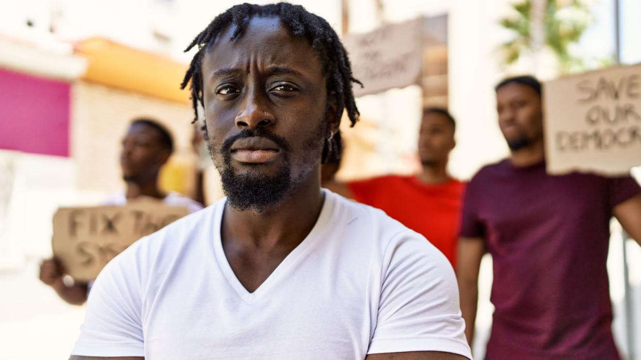 Black activist looking into the camera with several other Black men in the background holding protest signs