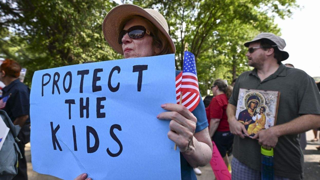 protect the kids sign held by protester with american flag