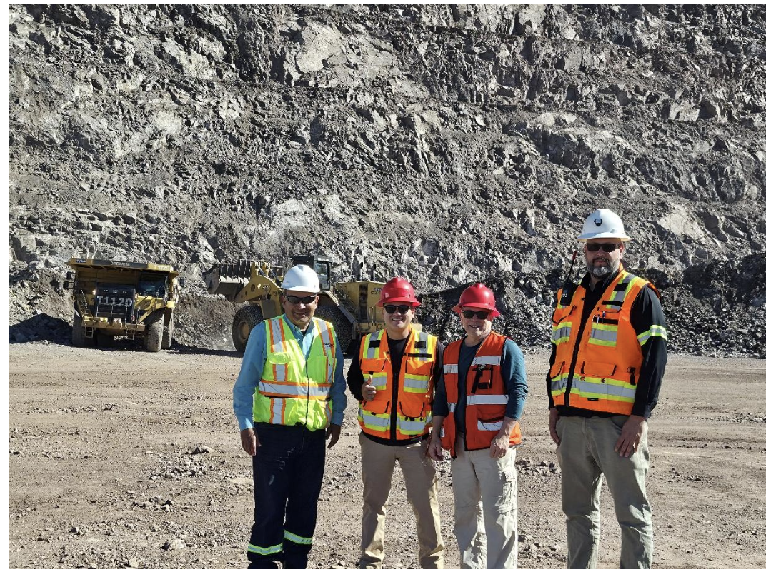 Goldgroup Mining's management team in front of dump trucks at a rocky construction site.