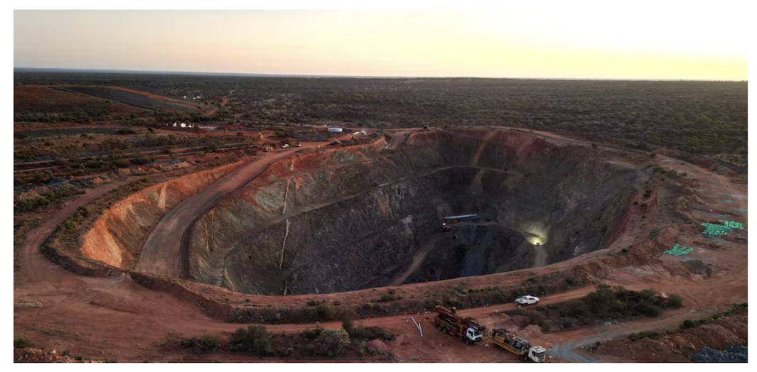 Aerial view of Brightstar Resources' vast open-pit mine at sunset, surrounded by a barren landscape.