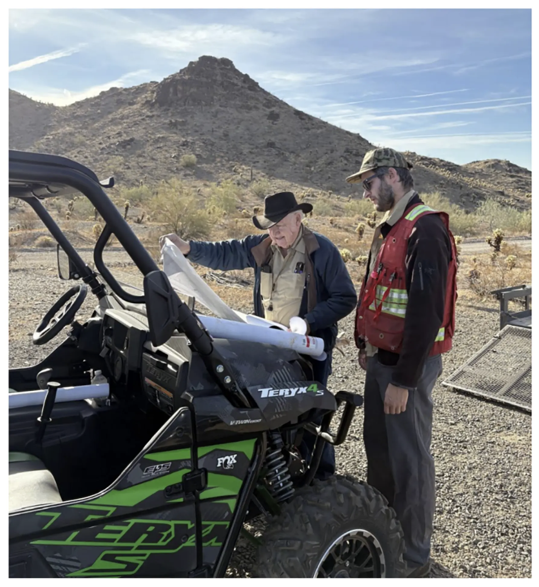 Two men examine a map over a green Teryx 4 off-road vehicle at Corcel Exploration's Yuma King project